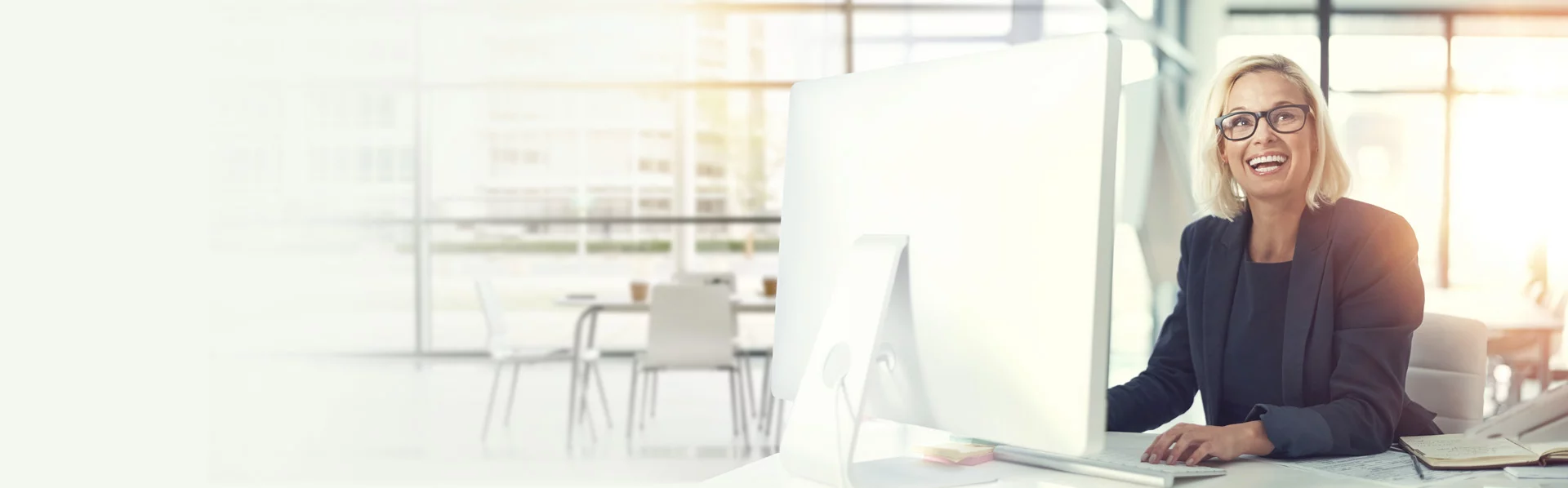 Lachende Geschäftsfrau am Schreibtisch vorm Laptop