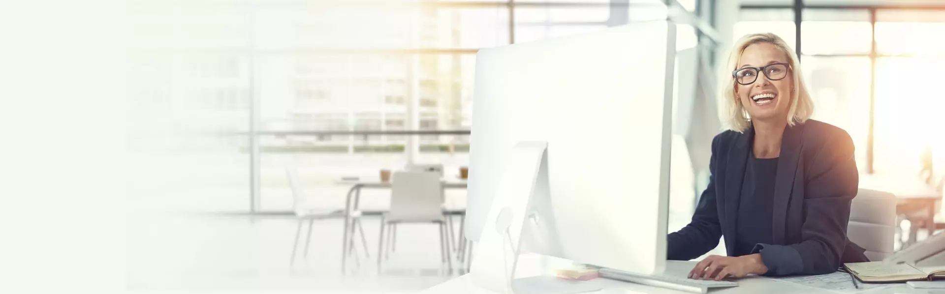 Lachende Geschäftsfrau am Schreibtisch vorm Laptop