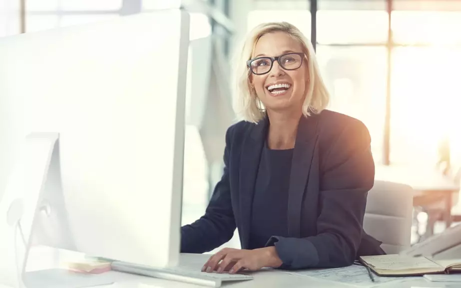 Lachende Geschäftsfrau am Schreibtisch vorm Laptop