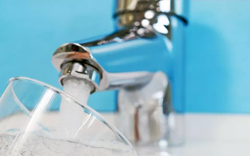 Wasser fließt aus einem Wasserhahn in ein Glas