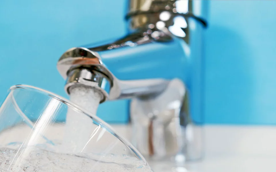 Wasser fließt aus einem Wasserhahn in ein Glas