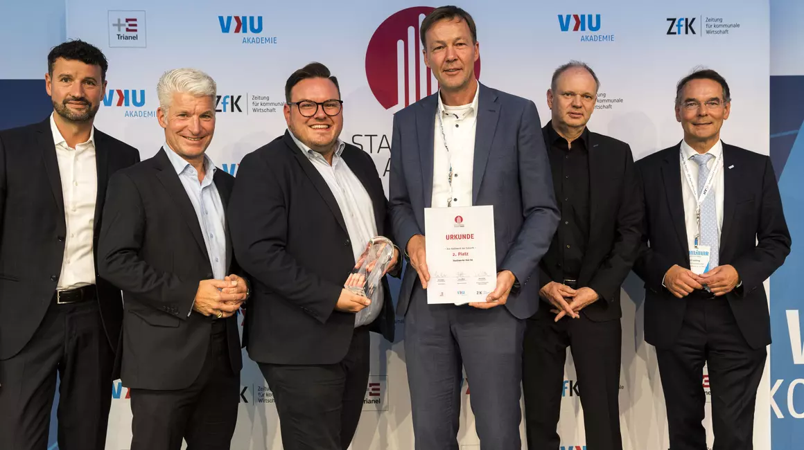 Kai Kistenmacher (4.v.li.), Leiter Privat- und Gewerbekunden bei den Stadtwerken Kiel, präsentiert die Urkunde für den zweiten Platz beim STADTWERKE AWARD 2022. (Foto: VKU Service GmbH)