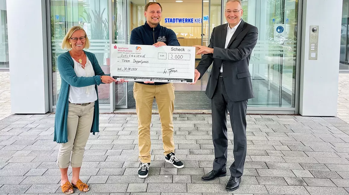 Aus 60 Millionen Schritten wird eine 2.000 Euro Spende: Technik- und Personalvorstand, Dr. Jörg Teupen (re.), übergibt gemeinsam mit Ideengeberin Gitte Küster den symbolischen Spendenscheck an Mirko Westphal vom Team DoppelPASS.
