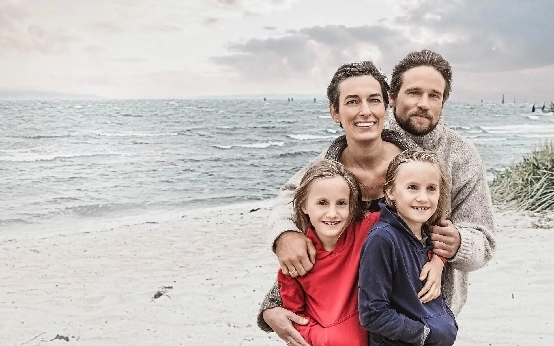 Sich umarmende Familie mit zwei Kindern bei stürmischem Wetter am Strand