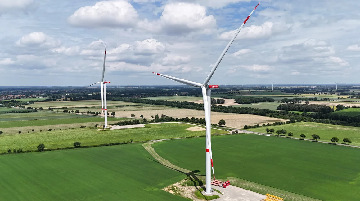 Zwei Windkraftanlagen auf grüner Wiese.
