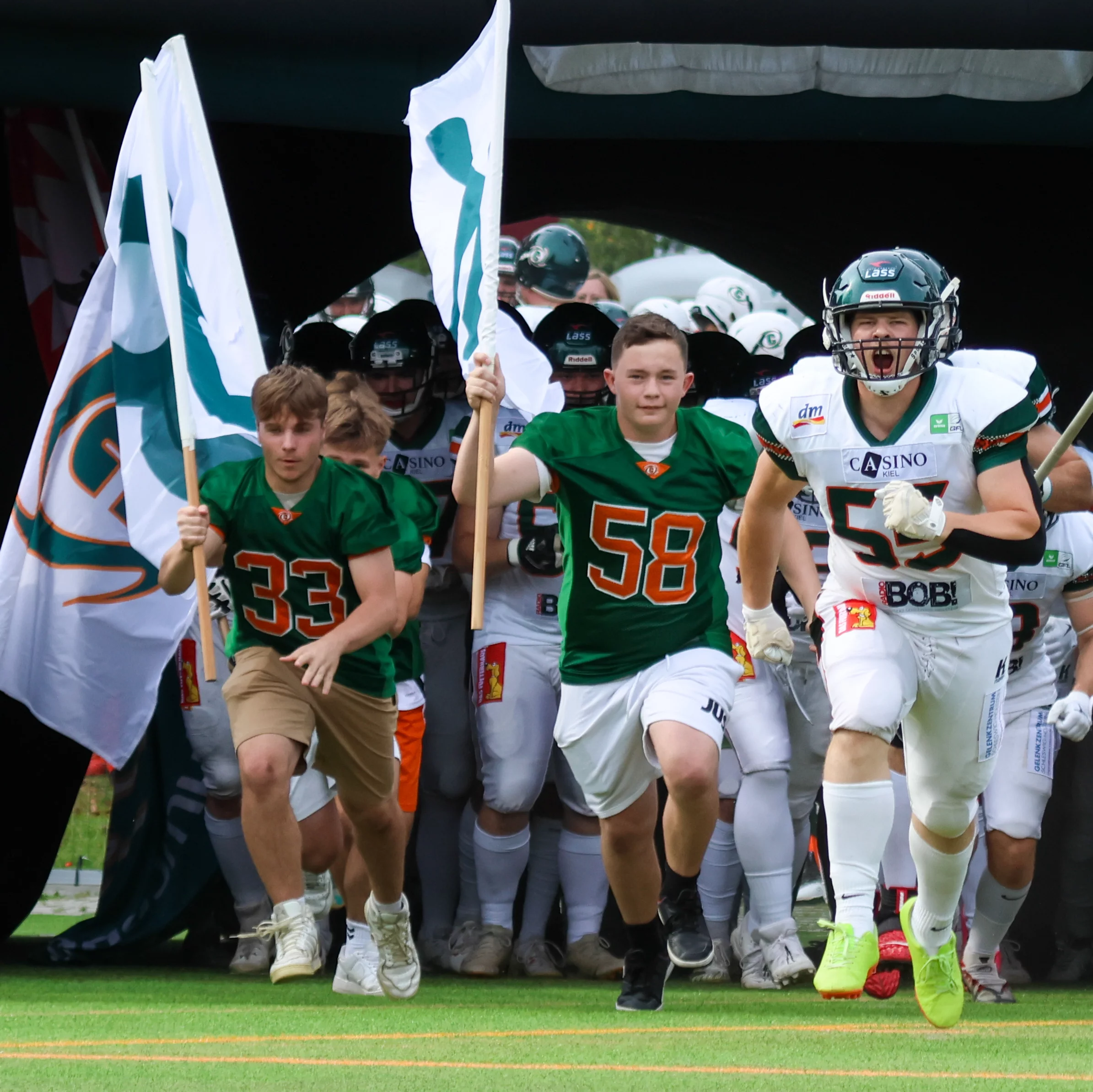 Spieler der Baltic Hurricanes laufen aus dem Tunnel auf das Spielfeld, begleitet von Teamfahnen und einem Banner. Ein dynamischer Moment vor Spielbeginn.