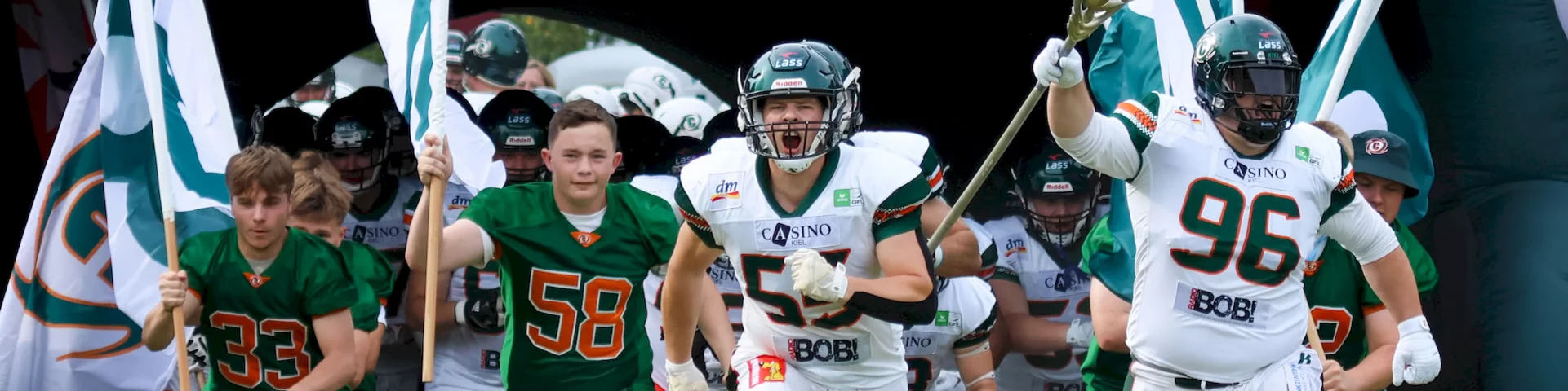 Spieler der Baltic Hurricanes laufen aus dem Tunnel auf das Spielfeld, begleitet von Teamfahnen und einem Banner. Ein dynamischer Moment vor Spielbeginn.