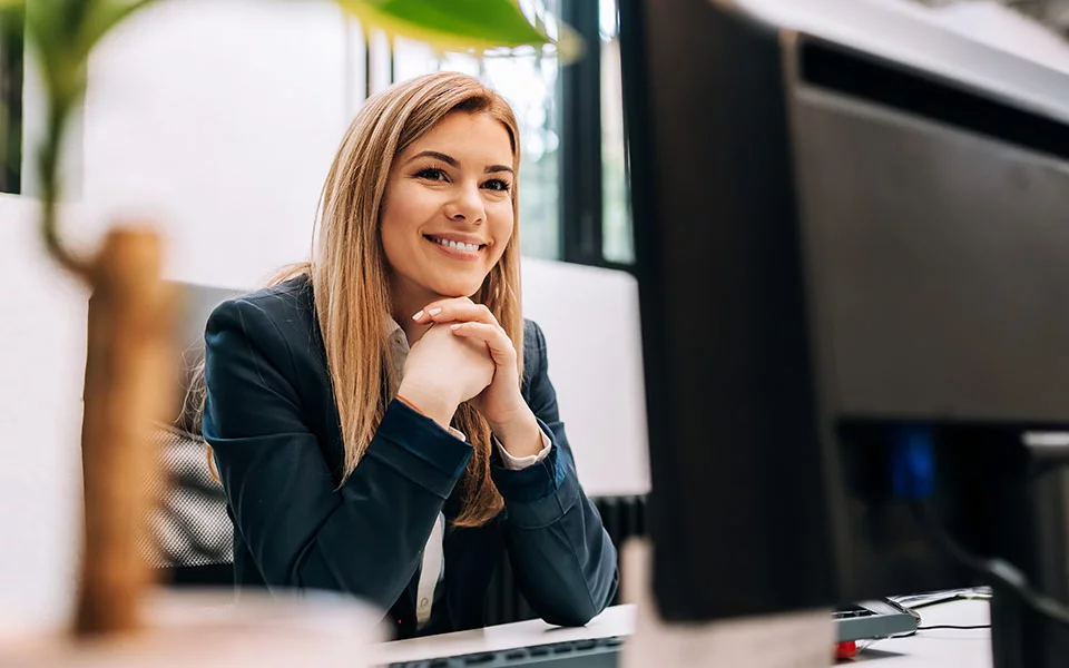 Gut gelaunte Mitarbeiterin sitzt am Schreibtisch vor Tastatur und Monitor